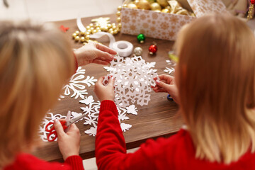 child with his mother carves snowflake for Christmas. family makes decorations for new year. Children's hands carve snowflake on background wooden table. Christmas theme. Selective focus. Rear view