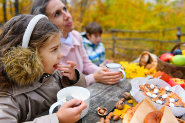 Obraz premium Portrait of a happy family in an autumn park. People are sitting at the table, eating and talking. Posing against the background of beautiful yellow trees. They are happy together.