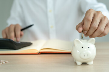 The man is putting two coins into his savings each month. A pig piggy bank holder and is show to the front as a symbol of savings. monthly savings concept.