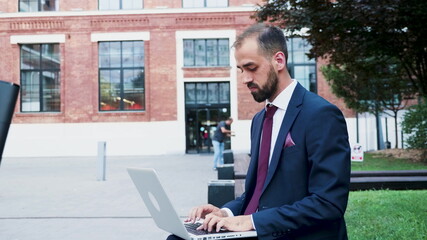 Leader woman sitting on bench holding laptop computer browsing business information preparing management presentation typing company strategy. Manager standing outside in front on startup office