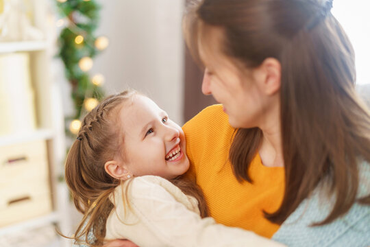 Happy Mother's Day. A little daughter congratulates her mother and snuggles up to her, wrapped in a blanket, sitting at home against the background of lights. Mom and girl smile and hug. Close-up