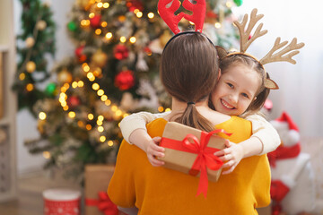 loving mother and daughter dressed in reindeer horns hug at home against background Christmas tree....