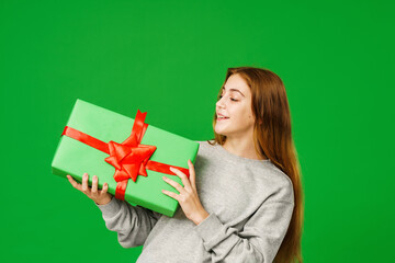 cute girl 13 years old with, standing with green gift boxes on a green background in studio. child smiles happily and looks into the frame. Advertising. copy space