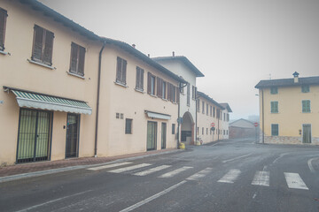 The street of a small Italian town Motella on a foggy winter day. Architecture of villages in northern Italy. Crosswalk. Facade of the beige house with closed shutters. 