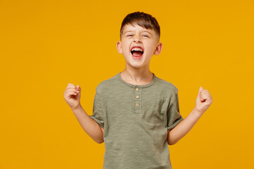 Full body little small fun happy boy 6-7 years old wearing green t-shirt sit in bag chair do winner gesture clench fist isolated on plain yellow background. Mother's Day love family lifestyle concept.