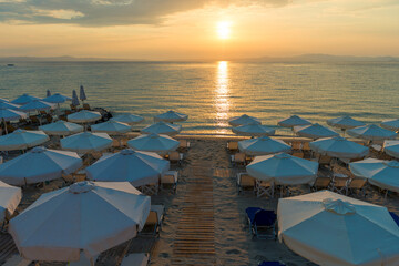 Obraz premium Beautiful sunset seascape with beach chairs and umbrella on the coast, Greece