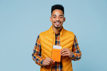 Traveler tourist cheerful happy young black man 20s years old wears yellow waistcoat shirt hold passport boarding tickets looking camera isolated on plain pastel light blue background studio portrait.
