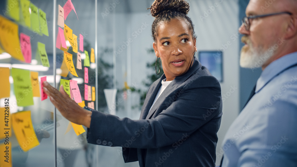 Poster senior manager talking to experienced businessman while creating time management plan on office wall