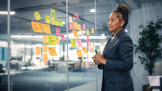 African American Businesswoman Creating Project Plan on Office Wall with Paper Notes. Stylish Confident Manager Working on Business, Financial and Marketing Projects. Specialist in Diverse Team.