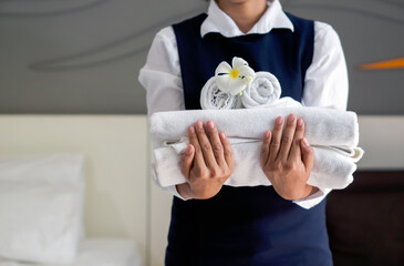 Closeup white towel with white flower on young hotel maid's hand. Staff in blue uniform preparing...