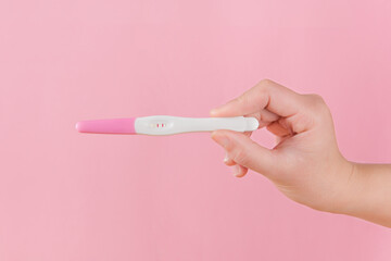 Woman is holding positive pregnancy test on pink background