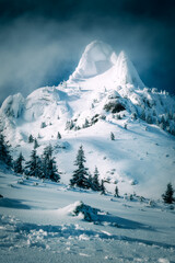 Beautiful view of an imposing and massive mountain peak covered with heavy snow against a blue sky with clouds