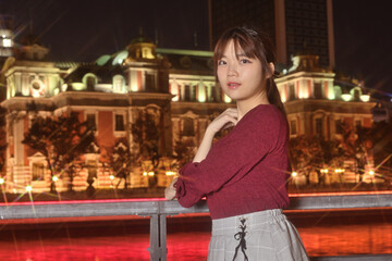 夜の公会堂を背にする女性