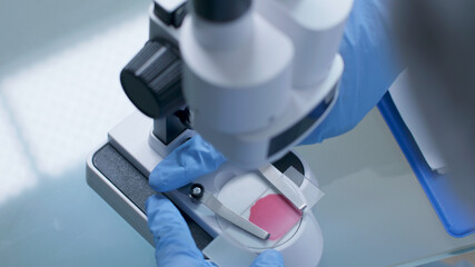 Closeup of scientist doctor hand adjusting medical microscope analyzing slide with blood sample working at vaccine development during chemistry experiment in hospital laboratory. Medicine concept