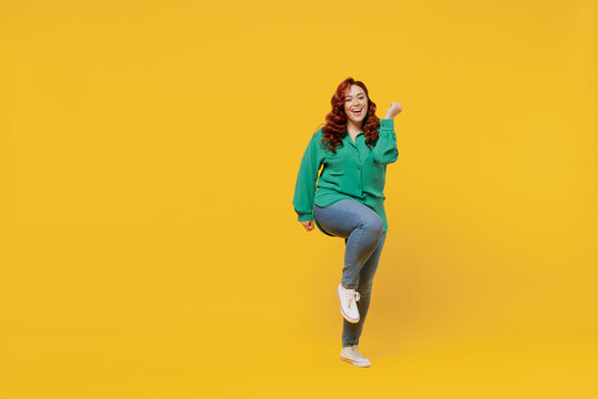 Full Size Body Length Happy Vivid Young Ginger Chubby Overweight Woman 20s Wears Green Shirt Doing Winner Gesture Celebrate Clenching Fists Say Yes Isolated On Plain Yellow Background Studio Portrait.