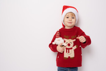 Little boy wearing santa hat holding santa claus toy standing over white background.