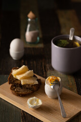 Still life breakfast. Boiled egg with salt, homemade bread with butter and cheese, tea. Front view.