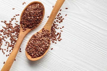Wooden spoons with flaxseed on a white wooden table.
