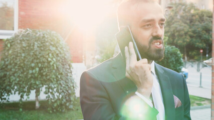 Businessman talking at modern phone discussing financial company with remote manager explaoning marketing strategy. Entrepreneur man standing outside in front on startup corporate office