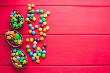 Chocolate easter eggs and colored sweets on a red wooden background. Place for text or logo.