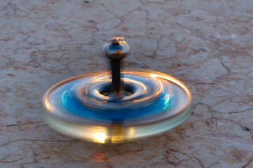 Fototapeta na wymiar A blue and gold glass Hanukkah dreidel sparkles as it spins on a stone surface in the afternoon sunlight. 