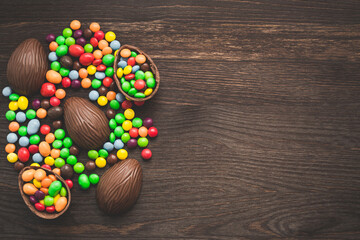 Chocolate easter eggs and colored sweets on a wooden background.