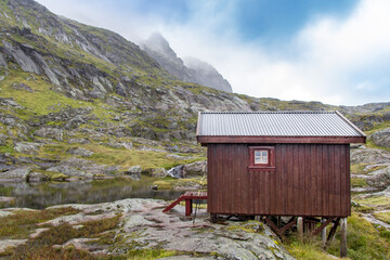 on single red hut in the rocks near a little lake with cloudy blue sky