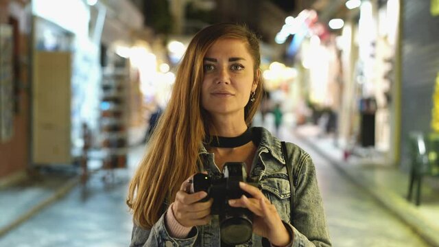 Female tourist photographer with camera, portrait face look. Leisure traveling vacation to Greece. Tourism time spending. Traveler woman on streets of Greek Athens. Cozy holidays dusk atmosphere.