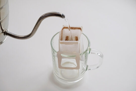 Drip bag coffee on glass cup. Pouring water from gooseneck kettle. Instant freshly brewing method