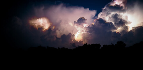 Fototapeta premium Electrical discharges of lightning in the night sky. Thunderclouds and lightning flashes during a thunderstorm at night. Panoramic photo.
