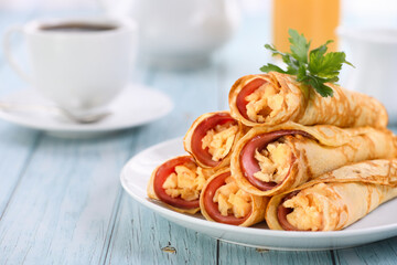 Homemade thin pancakes with a slice of ham and scrambled eggs, stacked in a stack, on the table. Great breakfast idea.