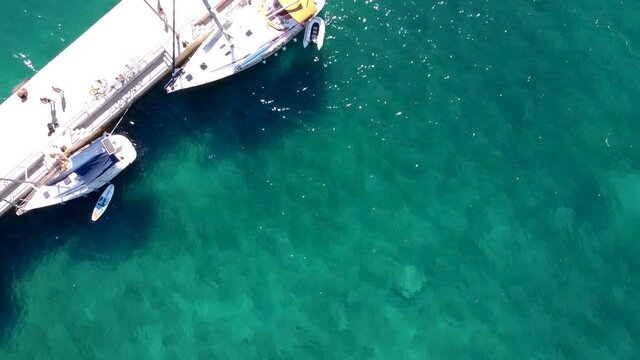 Aerial view of sailboats on the dock or peer and people on vacation. Boat is moored on island Olib in Croatia. Drone shot of tourists enjoying nautical tourism in Adriatic sea, resting on the pier.