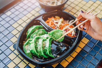Chopsticks with asian delicacy Gyoza or Jiaozi - fried dumplings. Green vegetarian or vegan food in...