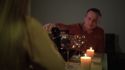 candlelight dinner at home. A man and a woman sit at a table on a date to celebrate valentine's day on february 14 or anniversary. The guy pours wine into a glass.