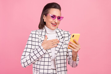 Portrait of cheerful lady in funky glasses hold hand chest see good news in smartphone isolated on...