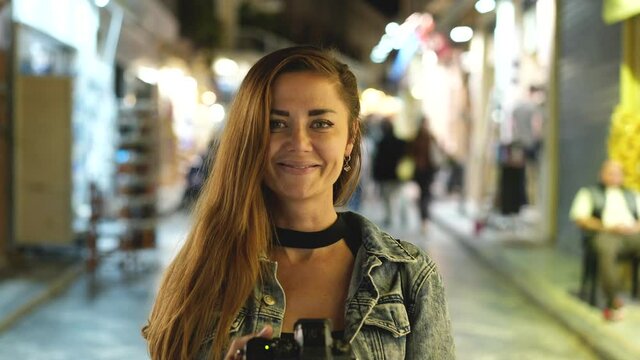 Female tourist photographer with camera, portrait face look. Leisure traveling vacation to Greece. Tourism time spending. Traveler woman on streets of Greek Athens. Cozy holidays dusk atmosphere.