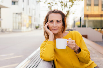 Smiling middle aged woman relaxing with coffee outdoors
