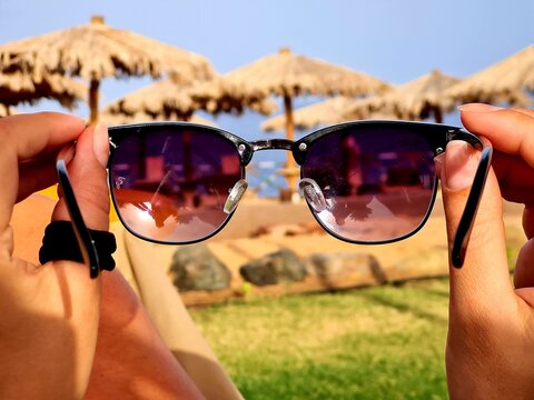 Hand holding sunglasses with brown lenses. The sunglasses at sunny summer day near the sea.