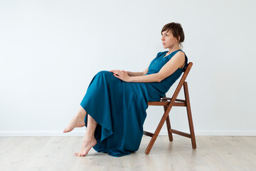  Woman in a long blue dress is naked, sits on a chair sideways 