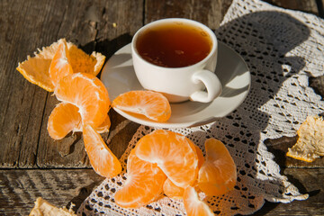 porcelain cup of tea on a saucer with tangerine slices on a wooden table.