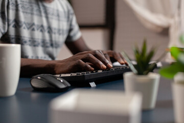 Closeup of african american young employee hand browsing management information typing project ideas on internet using computer sitting at desk in living room. Entrepreneur working remote from home © DC Studio