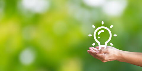 Hand holding light bulb icon on green background. Demonstrates energy savings and turns to solar...
