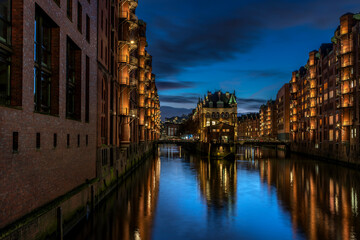 Detaillierte Panoramaaufnahme der beleuchteten Speicherstadt mit Wasserschloss  in Hamburg zur blauen Stunde und ein paar Wolken am Himmel (November 2021)