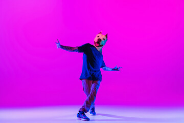 Young man, break dancing dancer headed of dog's head dancing isolated over bright magenta background at dance hall in neon light.