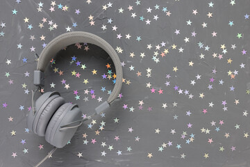 Headphones on festive black with stars confetti decoration background. Music, radio, podcasts, Christmas, New Year playlist concept. Top view, flat lay, copy space