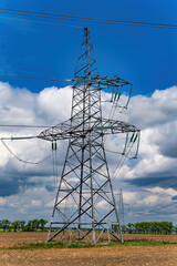 High-voltage power transmission tower with wires. High voltage line. Energy industry. Energy transfer. Blue sky. White clouds. Agricultural field. Cloudy horizon. Business. Electrician work.