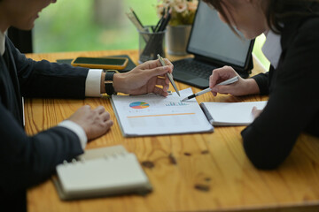 Close-up image of a business people meeting at a wooden table surrounded by paperwork, digital tablet and office equipment.