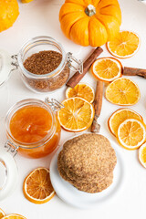 Aerial view of stacked shortbread cookies with orange slices, cinnamon, pumpkins and jam jar, on white table, vertical