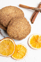 Aerial view of stacked shortbread cookies with orange and cinnamon slices, selective focus, on white table, vertical