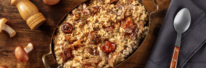 Mushroom risotto panorama, rustic mushrooms rice panoramic banner, top shot on a dark wooden background